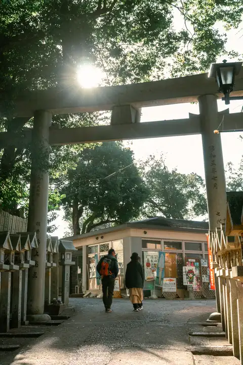Two people walking beneath a stone torii as sunlight breaks through the trees