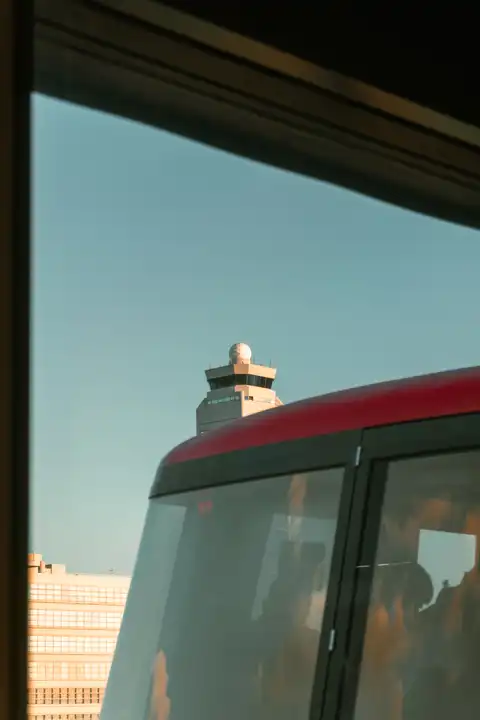 An airport control tower framed above a red bus in late afternoon light