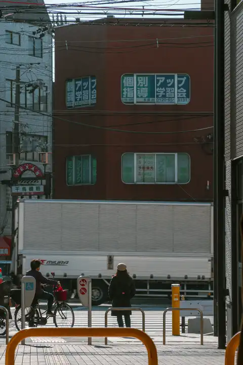 A cyclist and pedestrian waiting while a white truck crosses a Japanese street