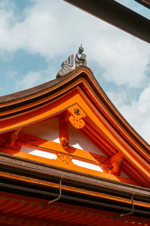 The layered orange roofline of a Japanese shrine against a pale blue sky