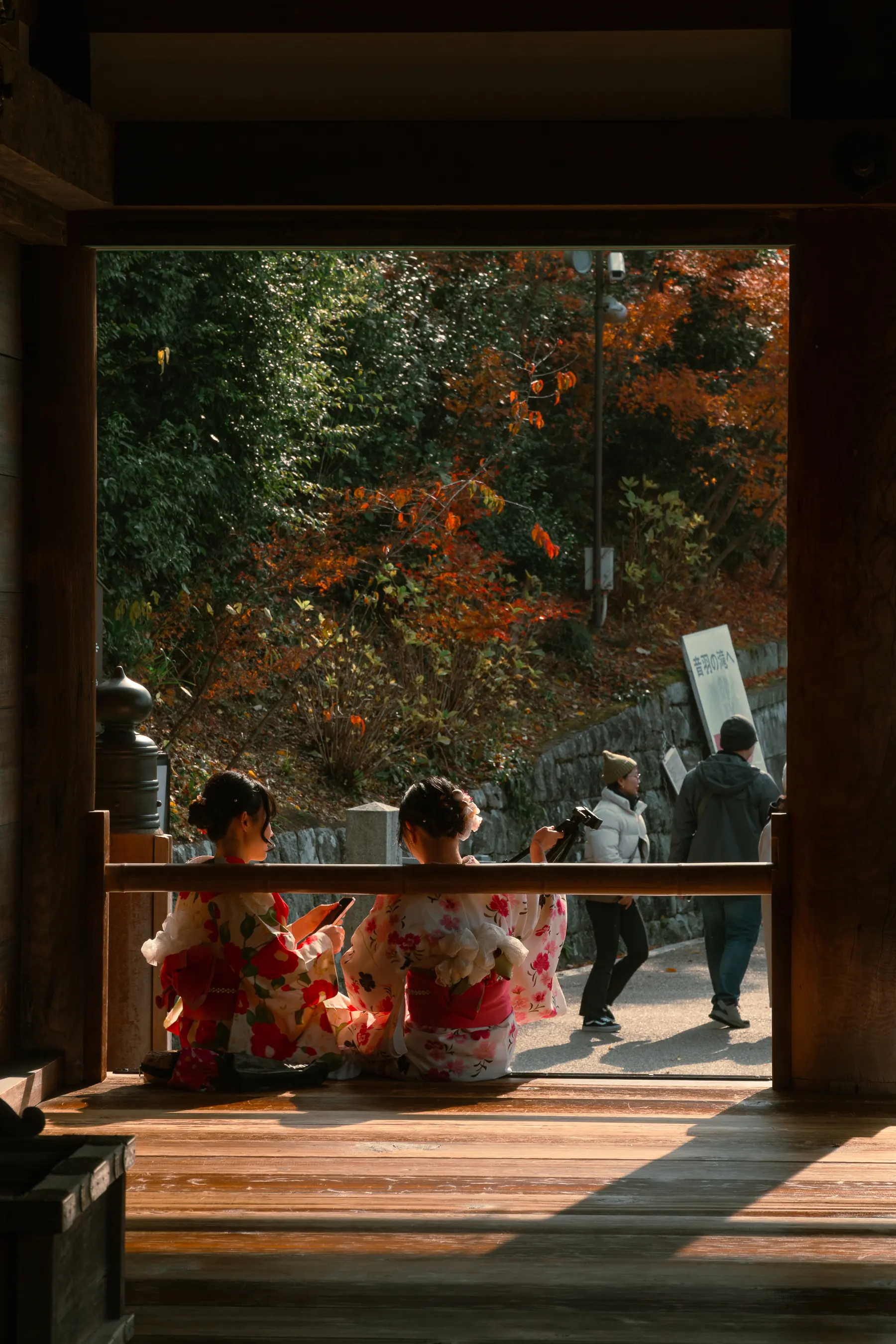 Two women in floral kimono seated inside a dark wooden doorway