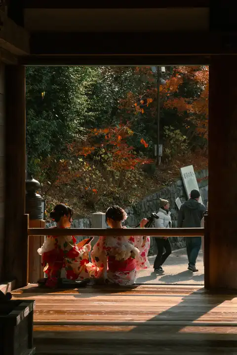 Two women in floral kimono seated inside a dark wooden doorway
