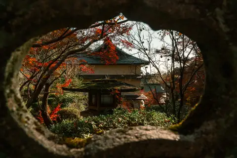 A temple garden and autumn leaves framed through a circular opening in a stone lantern