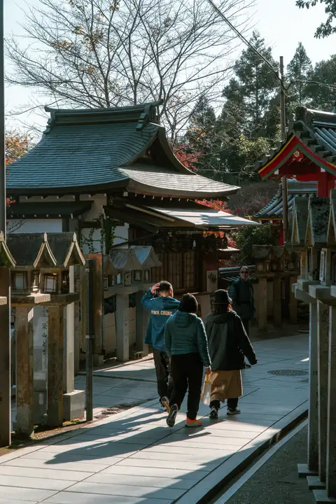 Two visitors walking down a narrow sunlit lane between shrine buildings