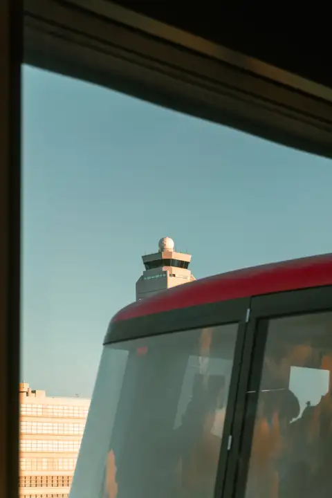 A red and white bus passing a distant observation tower, framed by a dark window
