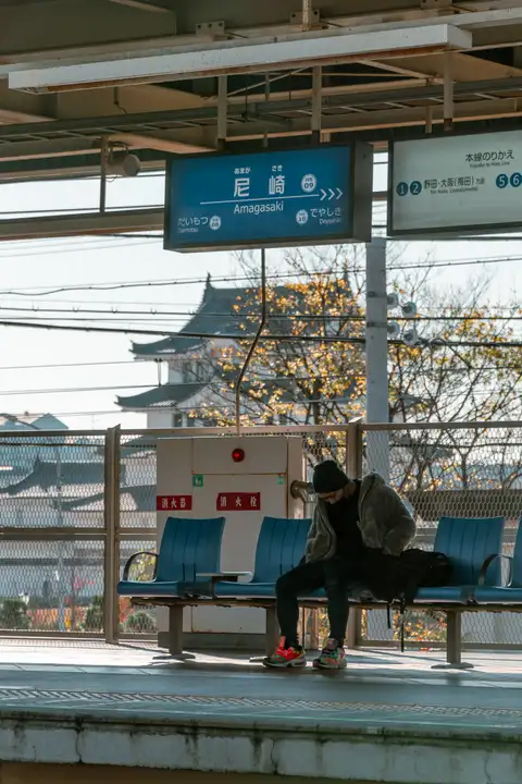A traveler seated on a station platform with a temple roof visible beyond the tracks