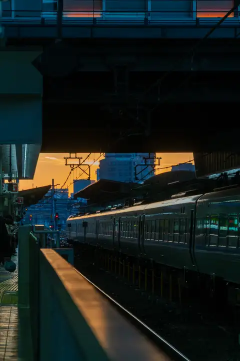 An empty station platform and train tracks beneath a blue overpass at dusk