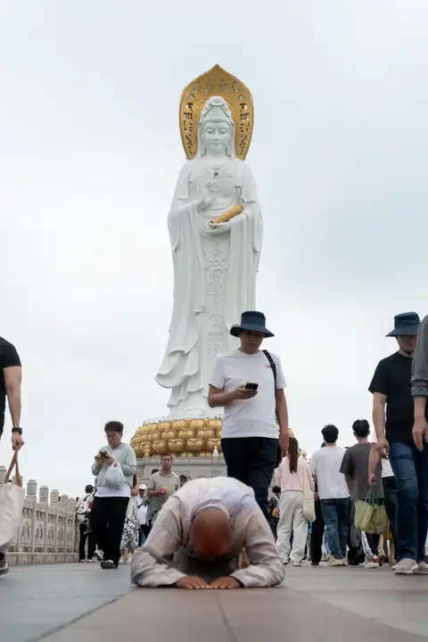 A worshipper prostrating on the approach to a monumental Guanyin statue