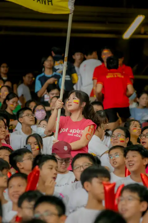 A student with red and yellow face paint holding a large flag among cheering schoolmates