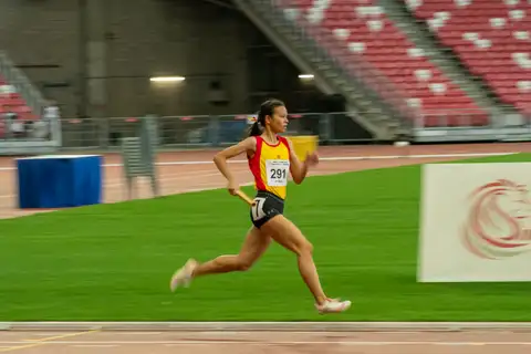 A Hwa Chong relay runner carrying a gold baton along the back straight