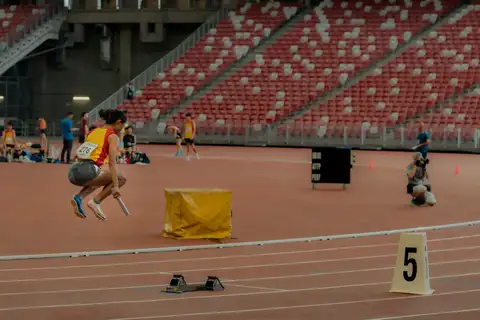 A Hwa Chong relay runner lifting both feet near the starting blocks while holding a baton