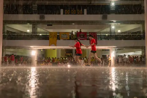 Two students in red shirts running hand in hand across a rain-soaked courtyard