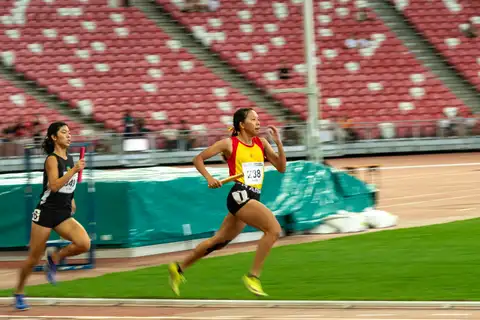 Two student relay runners racing closely together with batons on the back straight